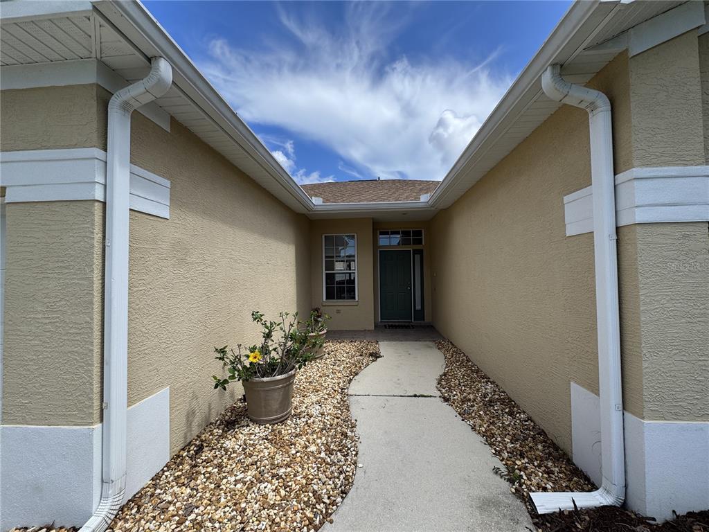 A concrete walkway leads to the front entrance of a tan house with white trim — 4815 50TH AVENUE W, BRADENTON, FL