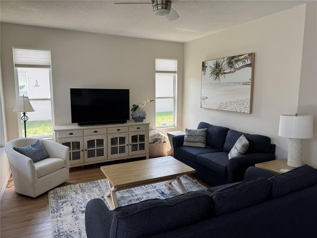A living room features a dark sofa, a light armchair, a television console, and area rug — 4815 50TH AVENUE W, BRADENTON, FL