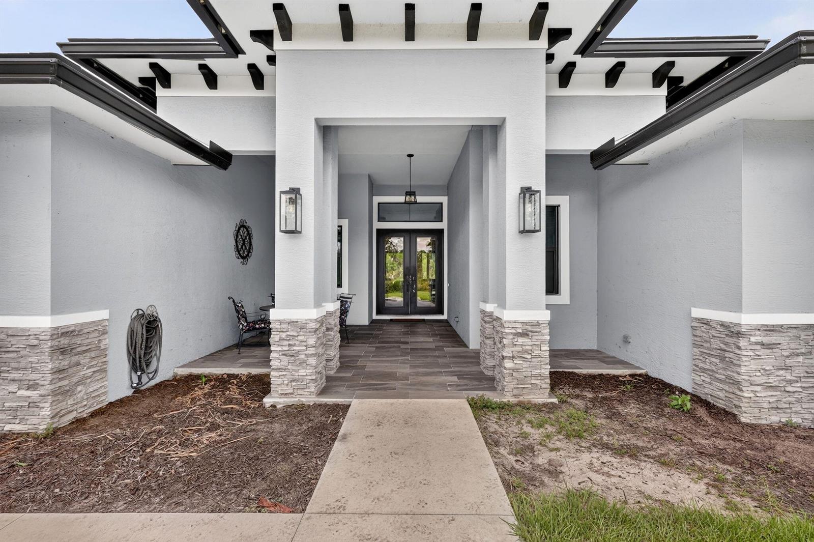 A modern house exterior features a covered entryway with stone pillars and double glass doors — 2643 Dyer Road, Fort Pierce FL 34952, FORT PIERCE, FL