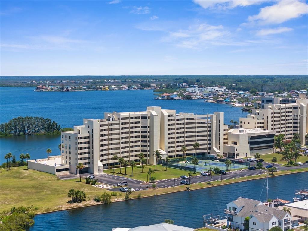 An aerial view shows a multi-story apartment building with a tennis court and parking lot — 5915 SEA RANCH DRIVE UNIT 211, HUDSON, FL