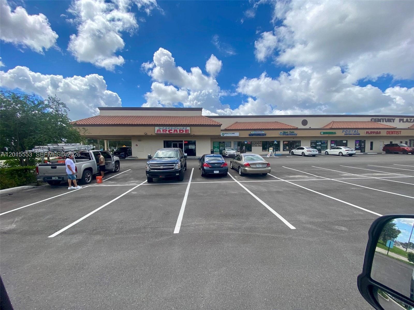 A parking lot in front of a strip mall with various storefronts under a cloudy sky — 5750 Okeechobee Blvd, FL 33417, FL