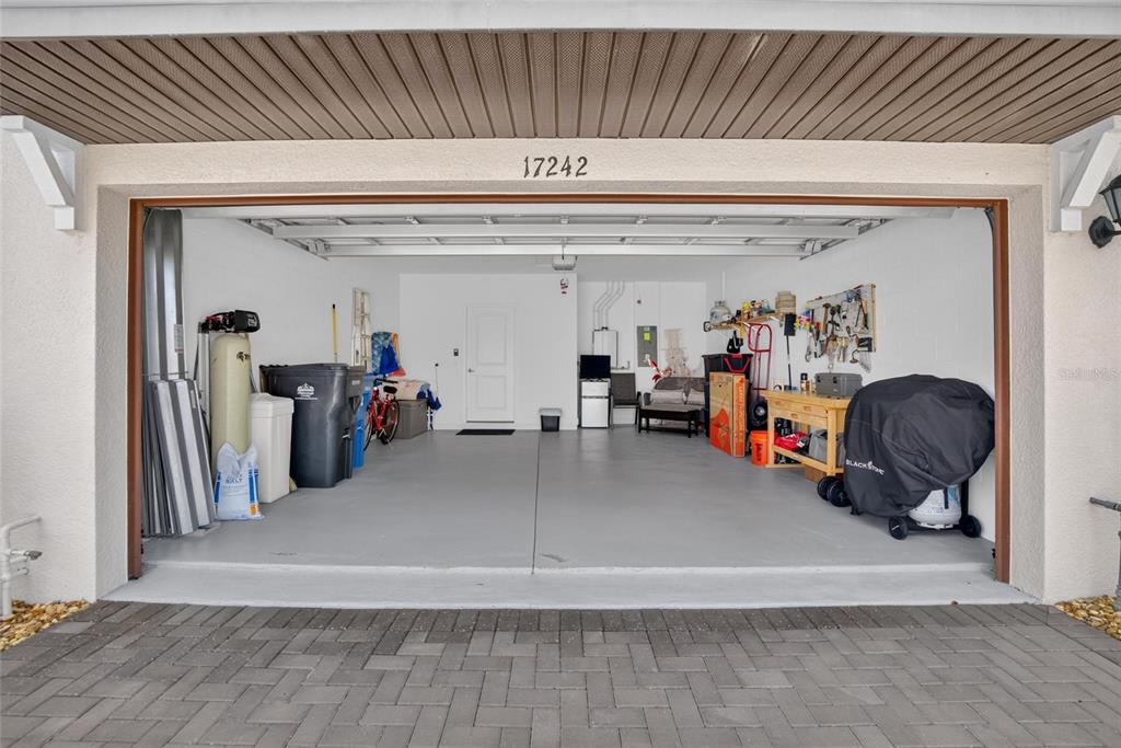 A two-car garage with a gray floor, white walls, and various storage items — 17242 HOLLY WELL AVENUE, WIMAUMA, FL