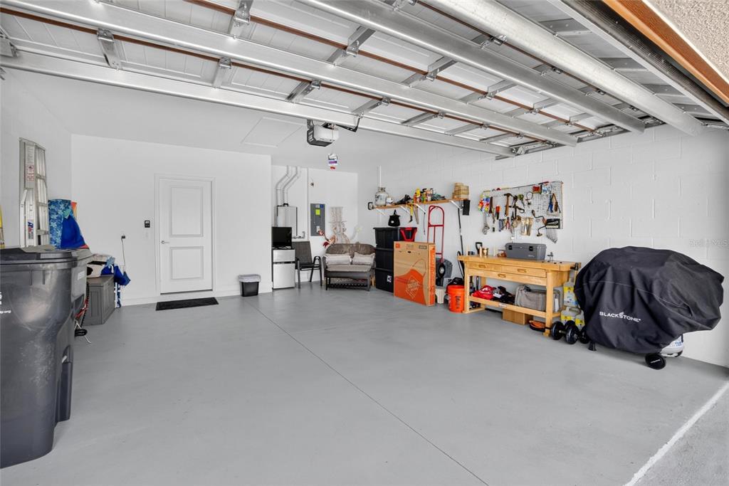 A garage with a gray floor, white walls, a workbench, and a covered grill — 17242 HOLLY WELL AVENUE, WIMAUMA, FL