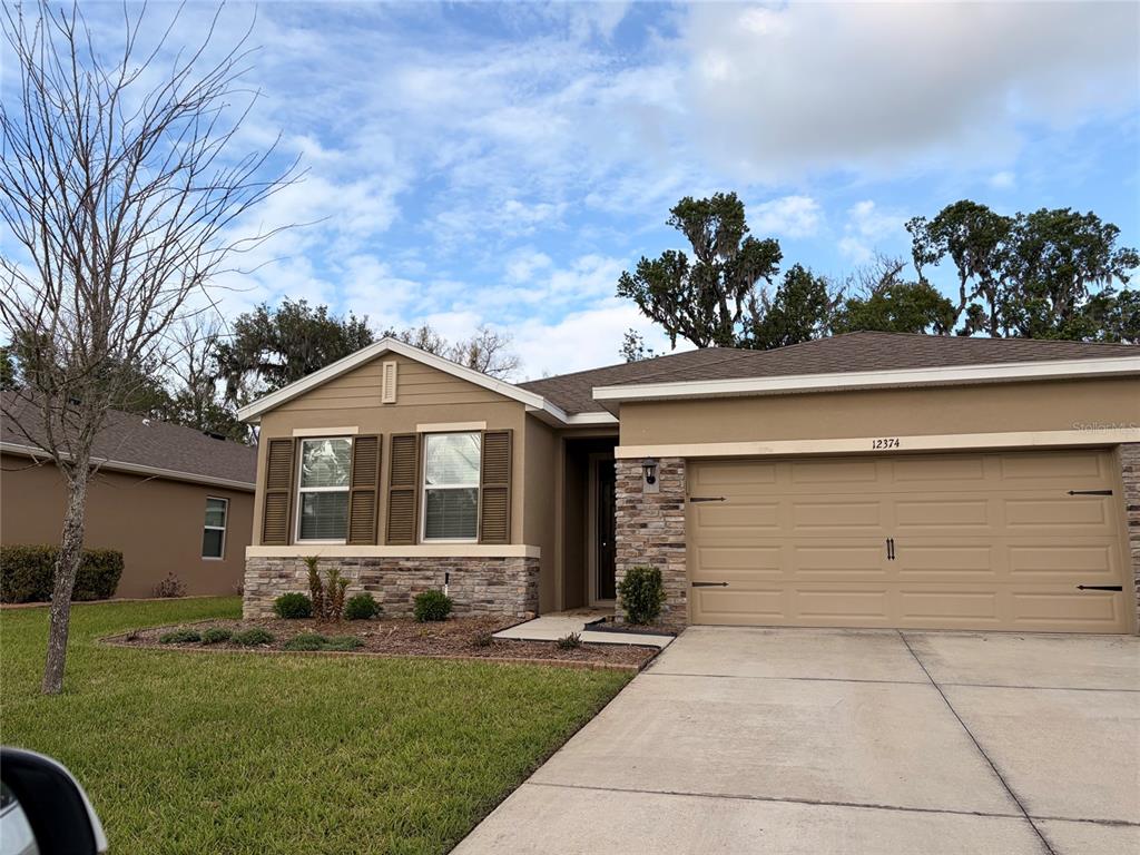 A single-story house with a tan stucco exterior, stone accents, and a two-car garage — 12374 EASTPOINTE DRIVE, DADE CITY, FL