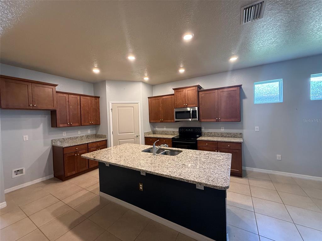 A kitchen features wood cabinets, granite countertops, a central island, and tile flooring — 12374 EASTPOINTE DRIVE, DADE CITY, FL