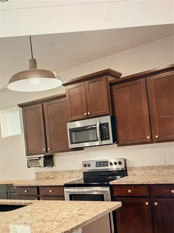 A kitchen features dark wood cabinets, stainless steel appliances, and speckled granite countertops — 12374 EASTPOINTE DRIVE, DADE CITY, FL