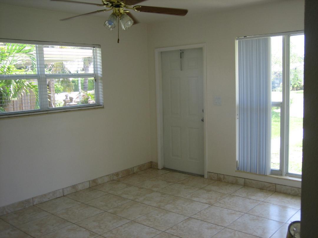 An empty room with beige tile flooring, a ceiling fan, a white door, and windows — 231 NE 24th Avenue # 1, Pompano Beach FL 33064, POMPANO BEACH, FL