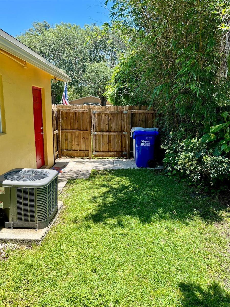 A backyard features a yellow house wall, an air conditioning unit, and a wooden fence — 231 NE 24th Avenue # 1, Pompano Beach FL 33064, POMPANO BEACH, FL