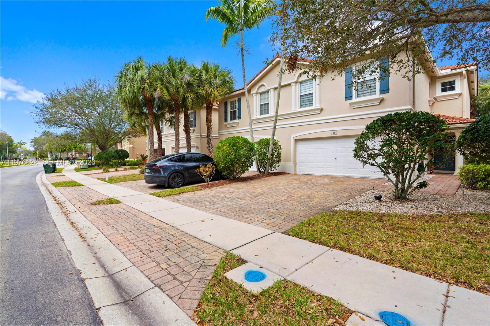 A two-story beige townhouse with a paved driveway, a white garage door, and palm trees — 4301 Macarthur Palm Trl, Green Acres FL 33463, GREEN ACRES, FL