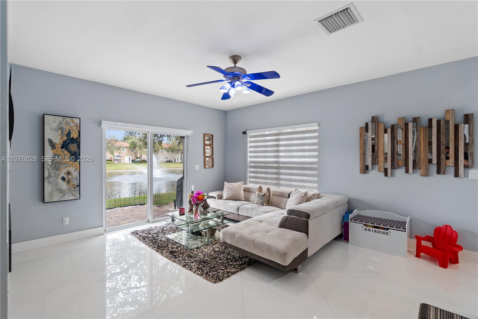 A living room features a sectional sofa, glass coffee table, and sliding doors overlooking a lake — 4301 Macarthur Palm Trl, Green Acres FL 33463, GREEN ACRES, FL