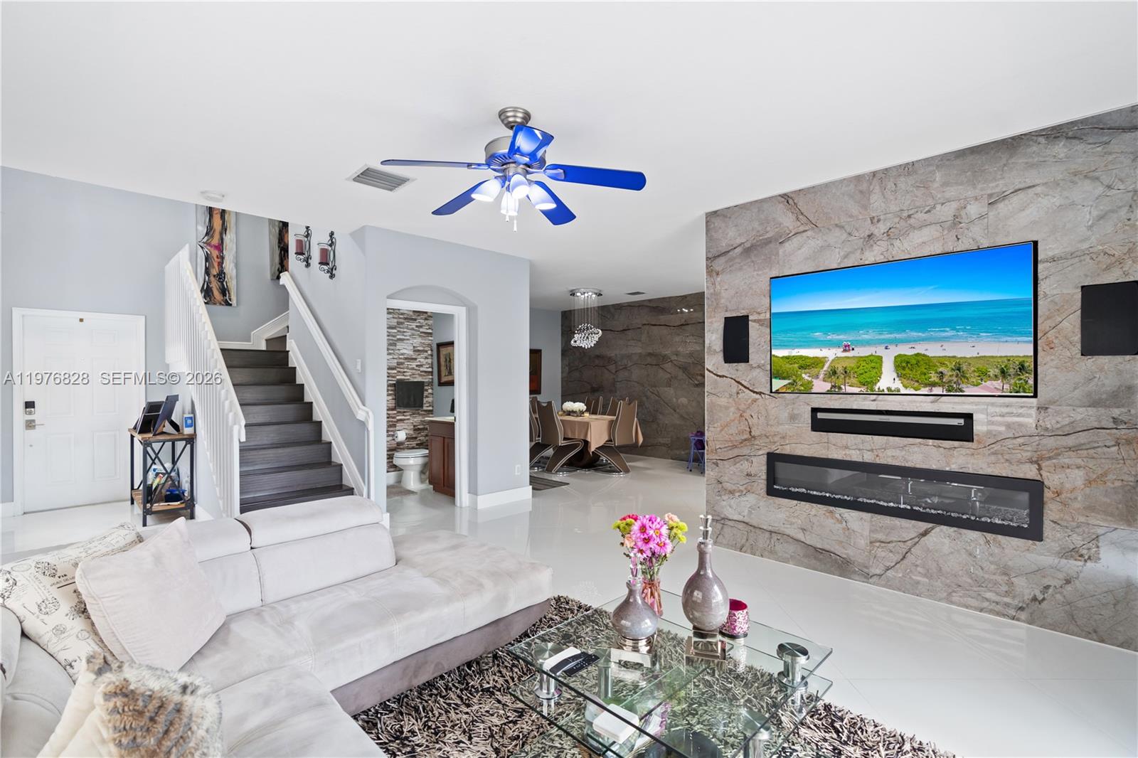 A living room features a stone-tiled fireplace wall, a television, and a glass coffee table — 4301 Macarthur Palm Trl, Green Acres FL 33463, GREEN ACRES, FL