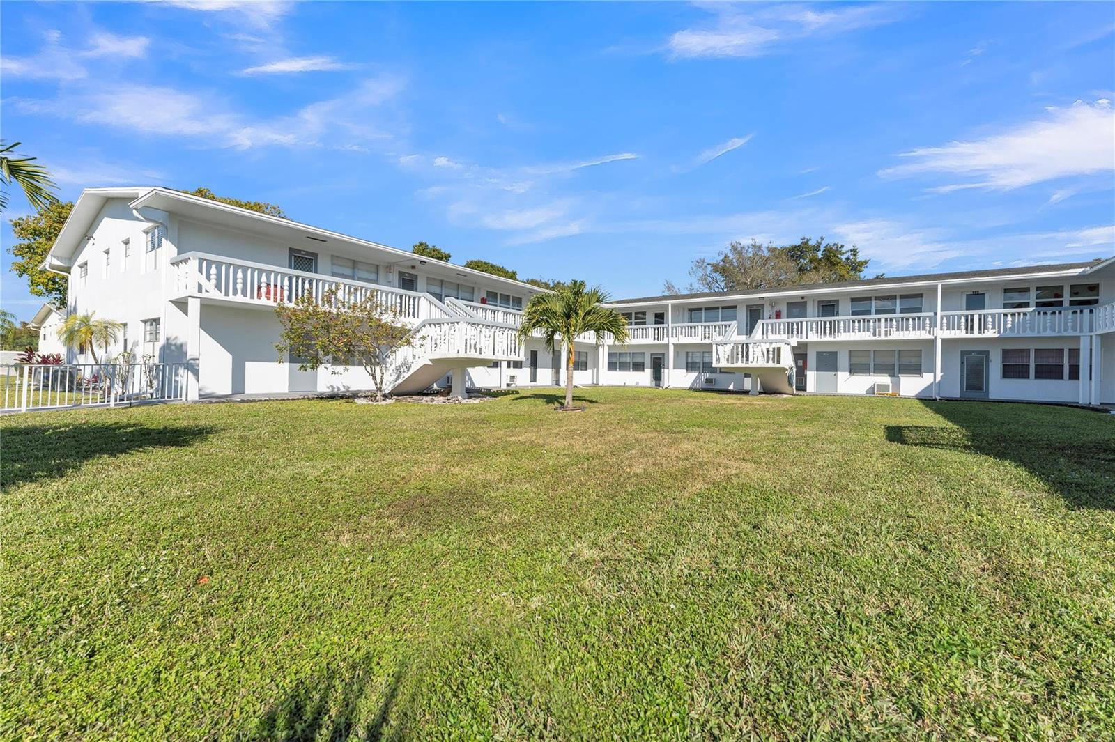A two-story white apartment building with exterior walkways and stairs faces a grassy courtyard — 176 Westbury J # 176, Deerfield Beach FL 33442, DEERFIELD BEACH, FL
