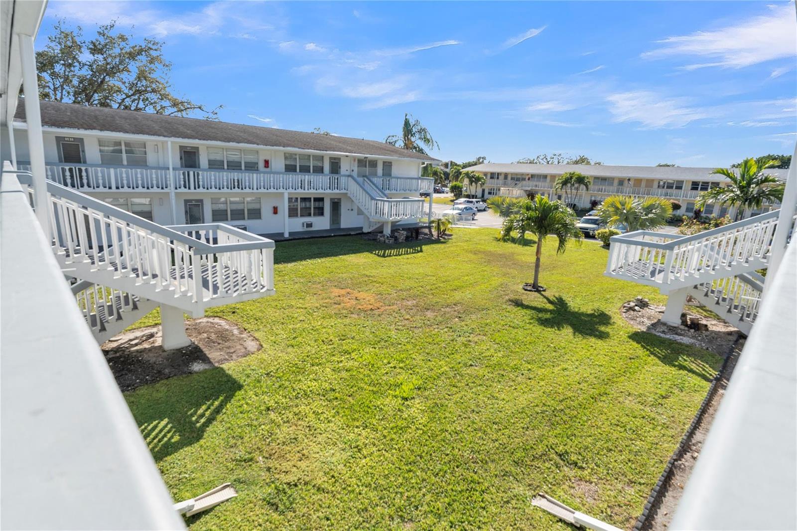 An exterior view of a grassy courtyard between two-story apartment buildings with white staircases — 176 Westbury J # 176, Deerfield Beach FL 33442, DEERFIELD BEACH, FL