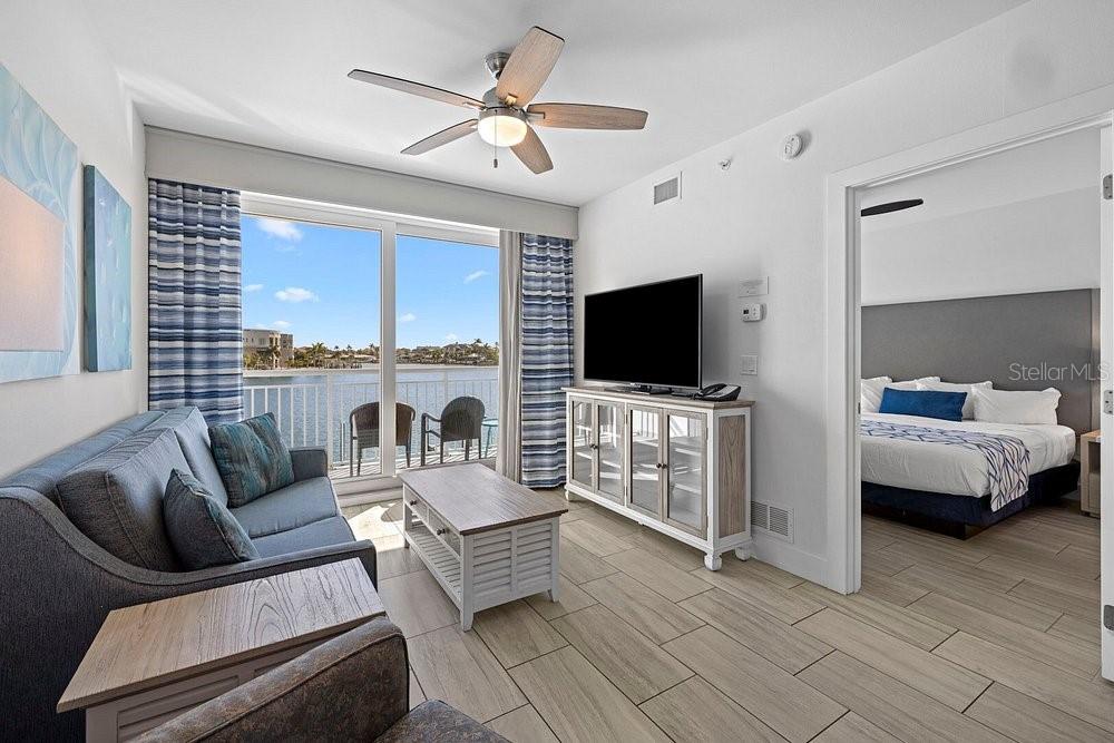 A living room with a sofa and coffee table leads to a balcony overlooking water — 10091 GULF BOULEVARD UNIT 203E, TREASURE ISLAND, FL