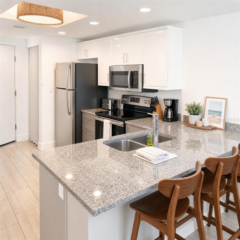 A kitchen features white cabinets, granite countertops, stainless steel appliances, and wooden bar stools — 10091 GULF BOULEVARD UNIT 203E, TREASURE ISLAND, FL