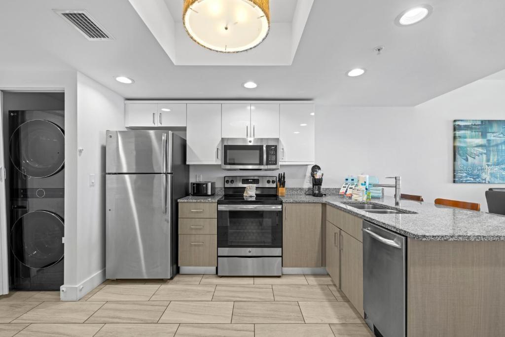 A modern kitchen features stainless steel appliances, white upper cabinets, wood-tone lower cabinets, and granite countertops — 10091 GULF BOULEVARD UNIT 203E, TREASURE ISLAND, FL