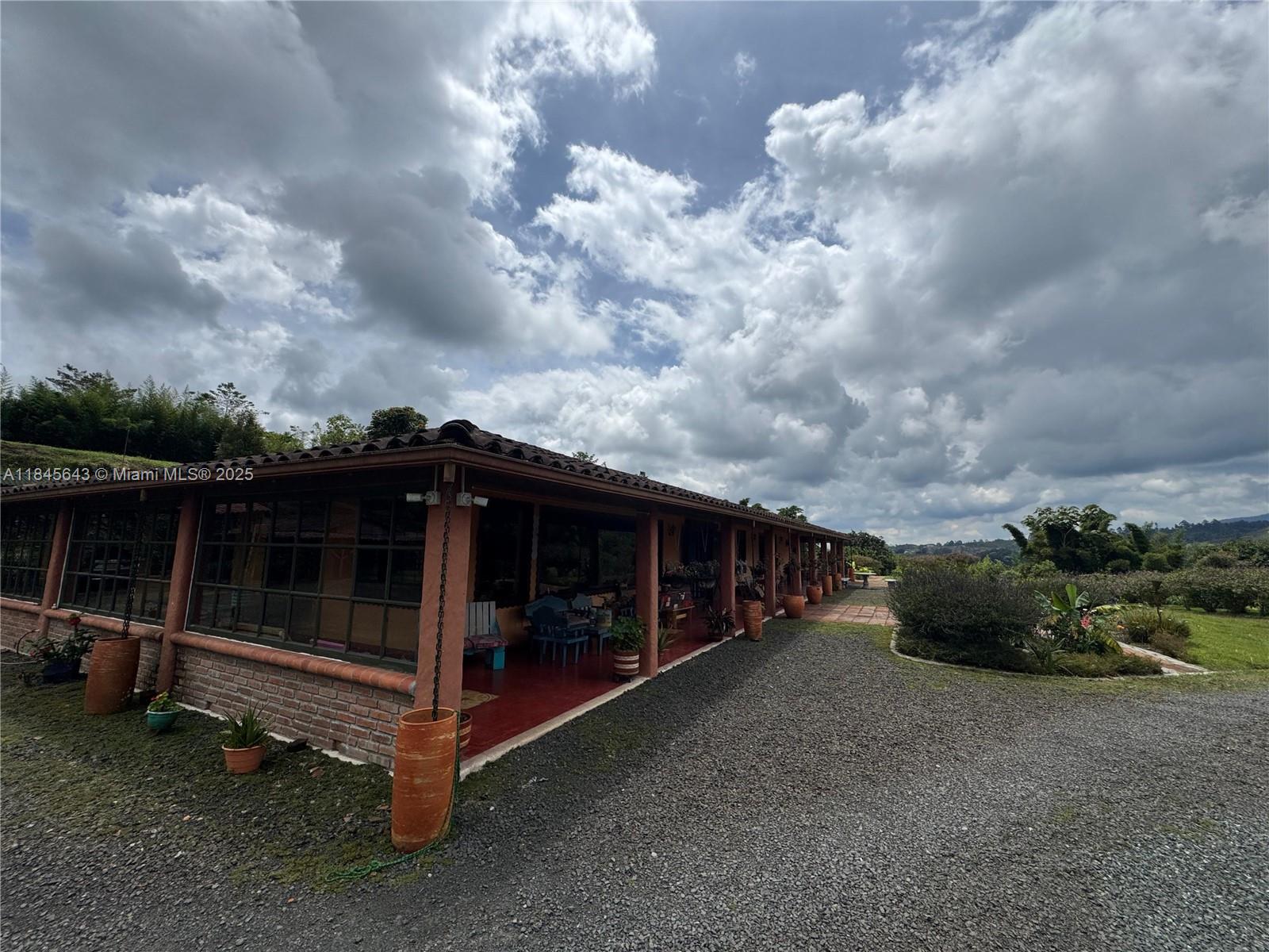 A long, single-story house with a covered porch and brick base sits on a gravel lot — 2222 via Filandia/Armenia, NA, NA