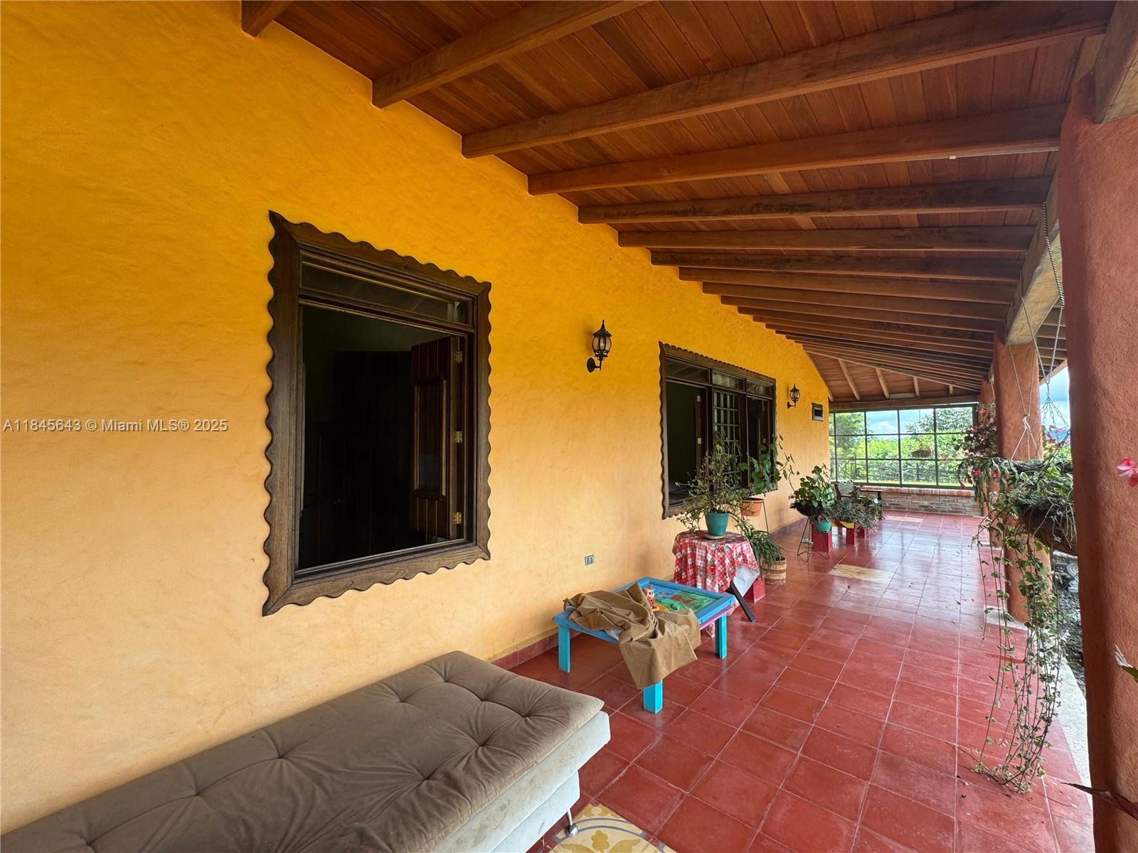 A covered outdoor patio features a yellow stucco wall, red tile flooring, and wooden beams — 2222 via Filandia/Armenia, NA, NA