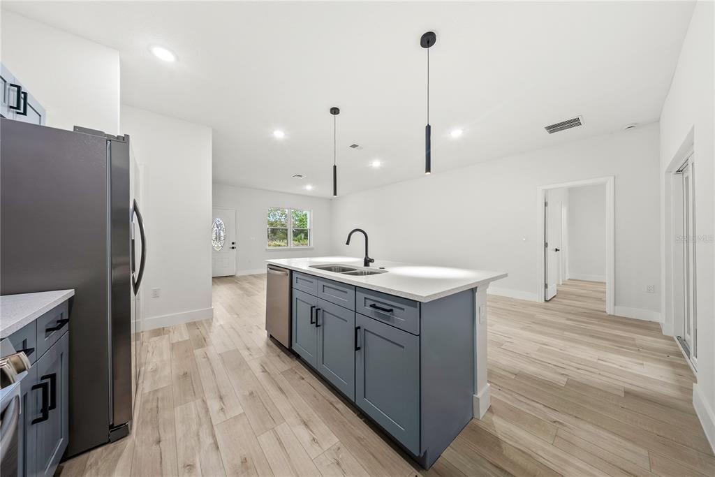 A kitchen features a blue island with a sink, stainless steel appliances, and light wood flooring — 3416 W EUNICE DRIVE, DUNNELLON, FL