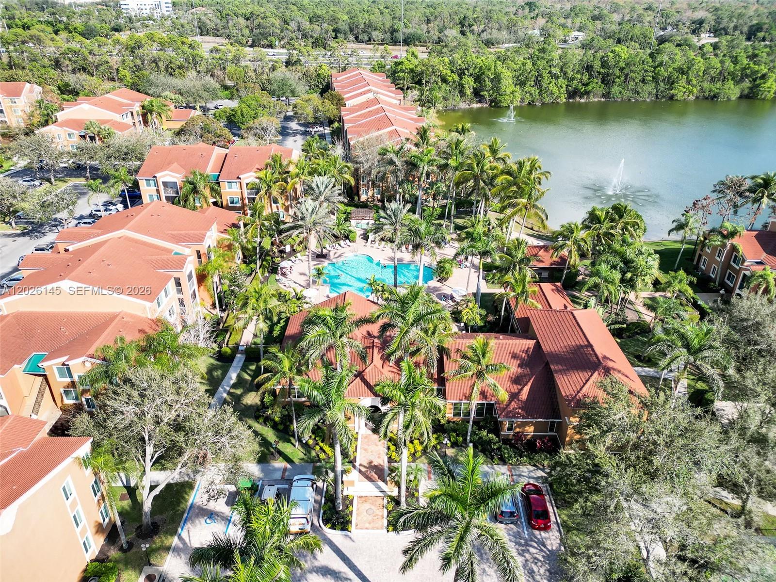 An aerial view shows a residential complex with a pool, lake, and palm trees — 1180 Reserve Way # 207, Naples FL 34105, NAPLES, FL