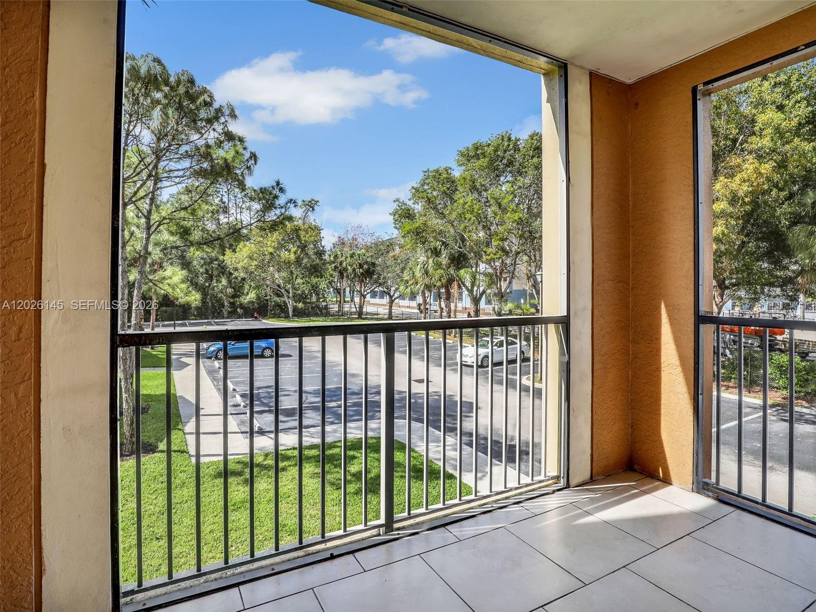 A tiled balcony with a metal railing overlooks a parking lot and trees — 1180 Reserve Way # 207, Naples FL 34105, NAPLES, FL