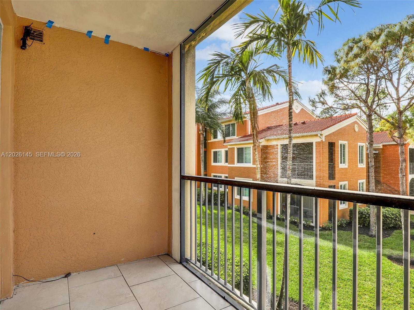 A tiled balcony with a metal railing overlooks a grassy courtyard and neighboring apartment buildings — 1180 Reserve Way # 207, Naples FL 34105, NAPLES, FL