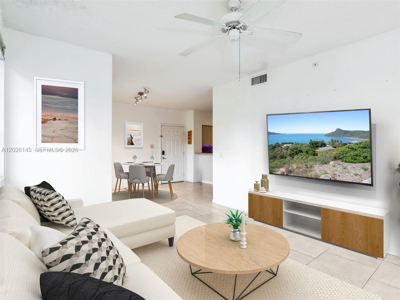 A living room features a white sectional sofa, a round coffee table, and a wall-mounted television — 1180 Reserve Way # 207, Naples FL 34105, NAPLES, FL