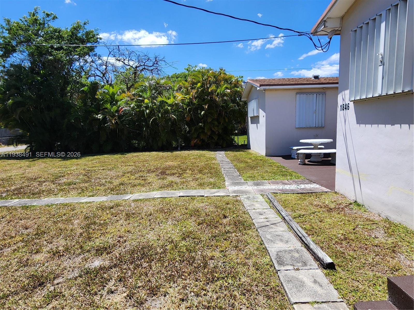 A backyard features a grassy lawn, a stone walkway, and a small building with a table — 1846 Wiley St, Hollywood FL 33020, HOLLYWOOD, FL