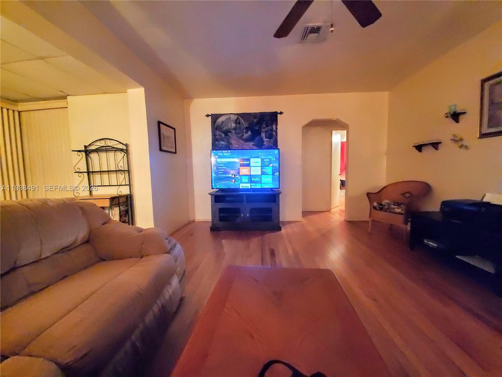 A living room features hardwood floors, a television on a stand, and a beige sofa — 1846 Wiley St, Hollywood FL 33020, HOLLYWOOD, FL