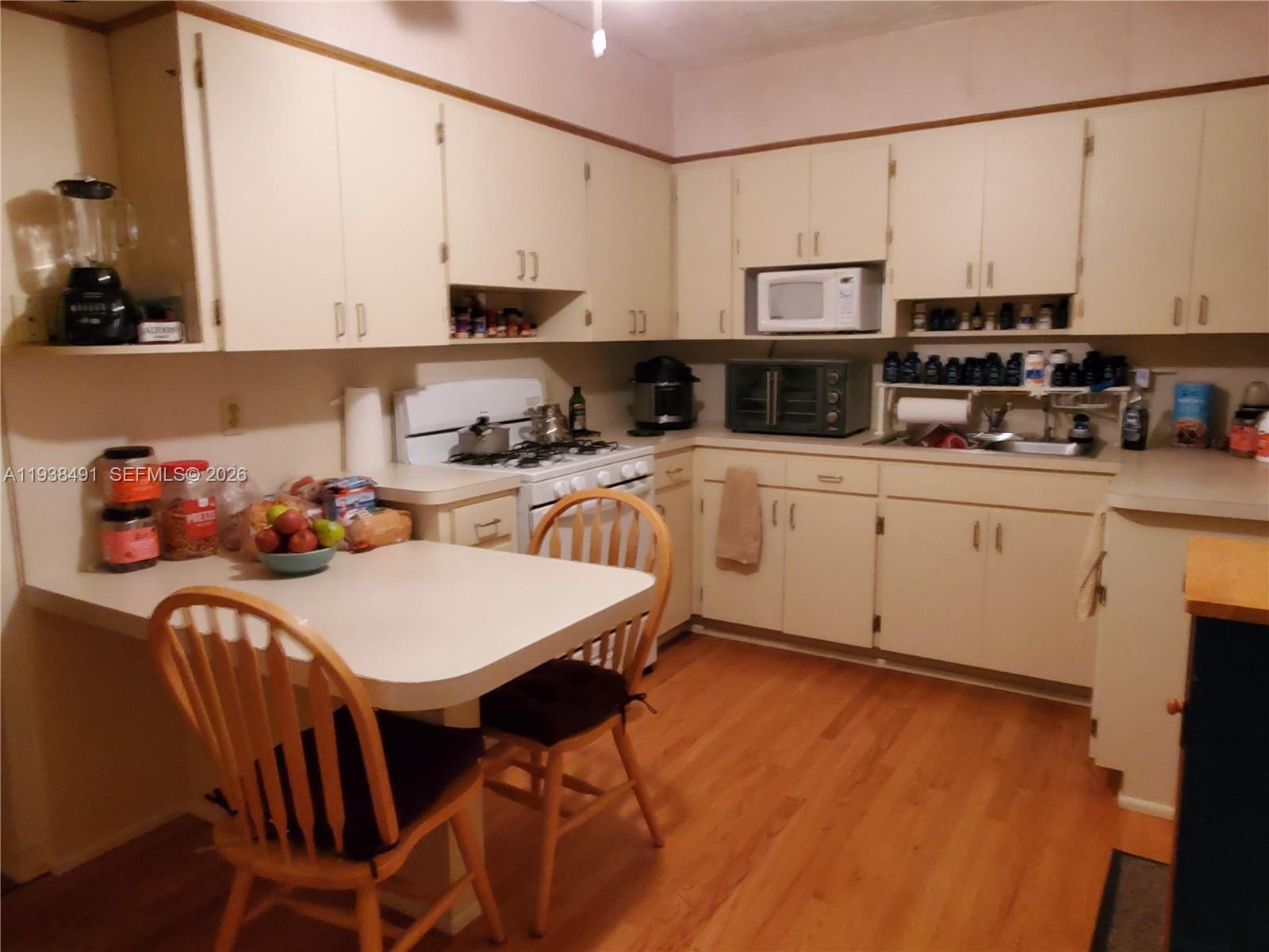 A kitchen features light-colored cabinets, a small dining table with two chairs, and wood flooring — 1846 Wiley St, Hollywood FL 33020, HOLLYWOOD, FL