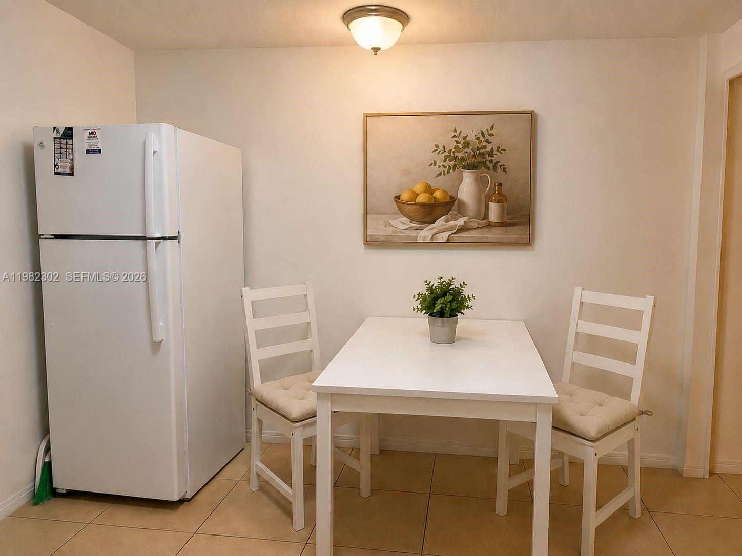 A white refrigerator stands next to a small dining table with two chairs — 2620 SW 51st St # 2, Dania Beach FL 33312, DANIA BEACH, FL