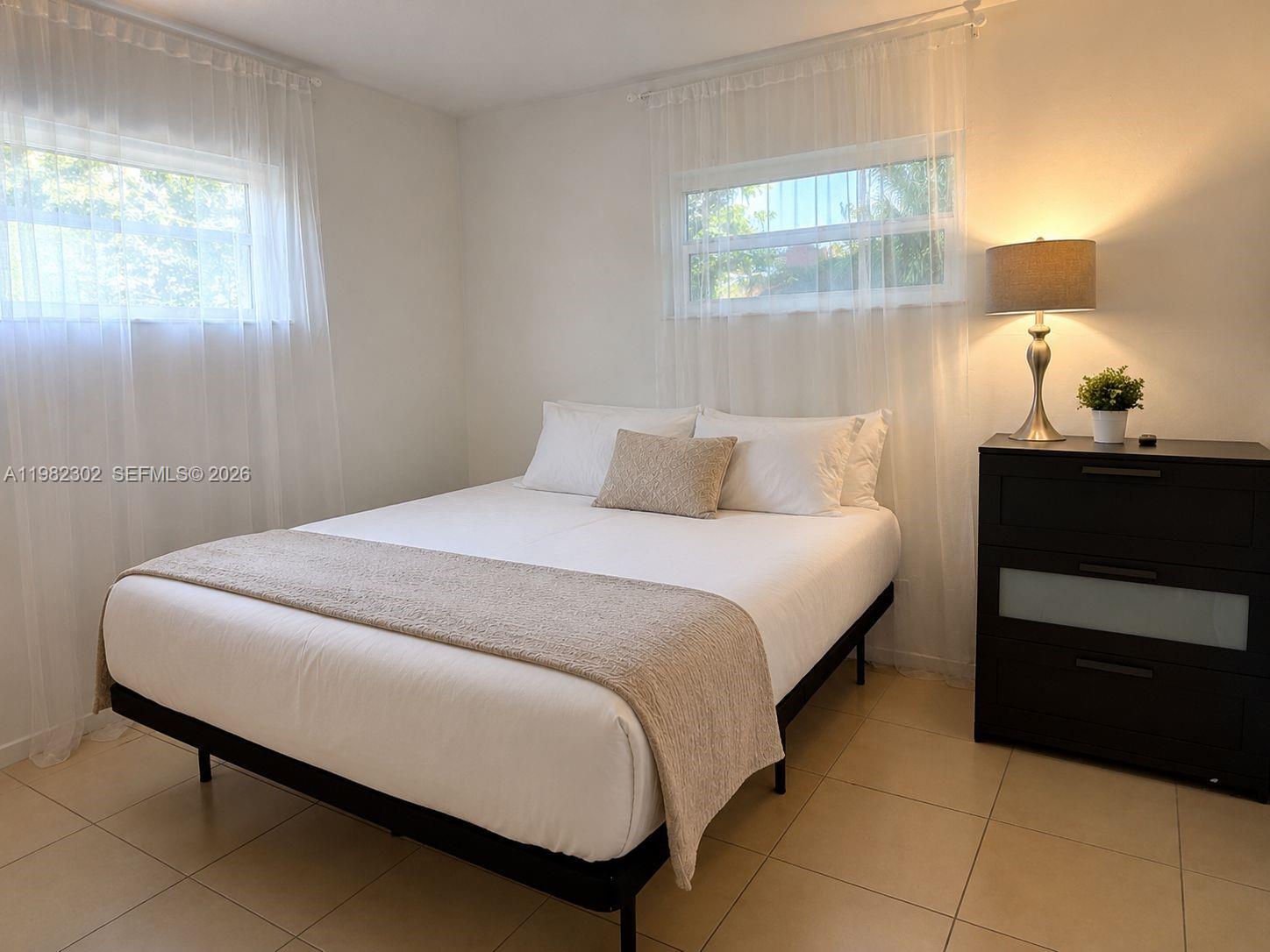 A bedroom features a bed with white linens, a dark dresser, and two windows — 2620 SW 51st St # 2, Dania Beach FL 33312, DANIA BEACH, FL