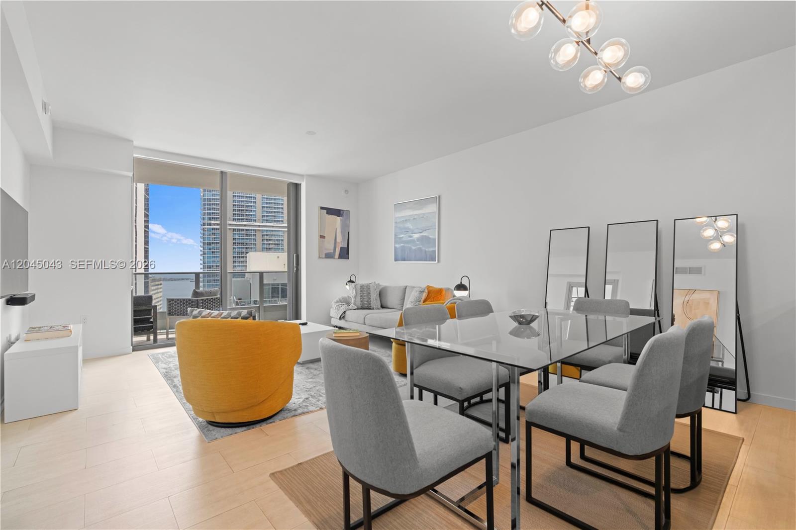 A modern living and dining area features a glass table, gray chairs, and a yellow armchair — 1000 E Brickell Plz # 3803, Miami FL 33131, MIAMI, FL