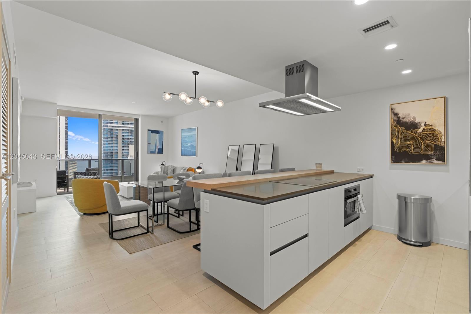 A modern kitchen island with a wooden breakfast bar overlooks a dining and living area — 1000 E Brickell Plz # 3803, Miami FL 33131, MIAMI, FL