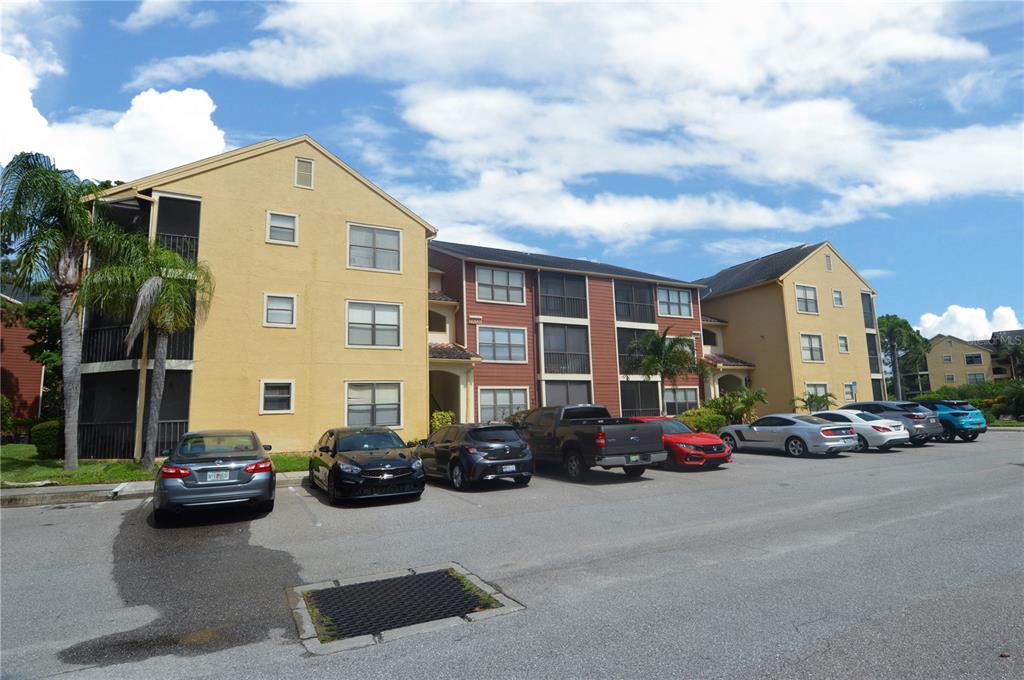 A three-story apartment building with yellow and red siding stands behind a paved parking lot — 11901 4TH STREET N UNIT 10206, ST PETERSBURG, FL