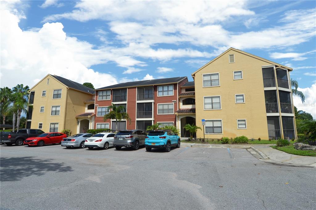 A three-story apartment building with yellow and red siding stands behind a paved parking lot — 11901 4TH STREET N UNIT 10206, ST PETERSBURG, FL