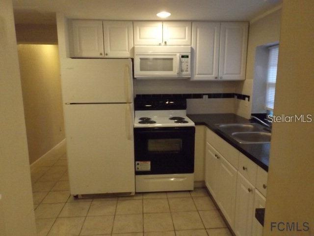 A kitchen with white cabinets, a white refrigerator, a black stove, and tiled flooring — 5150 N OCEAN SHORE BOULEVARD, PALM COAST, FL
