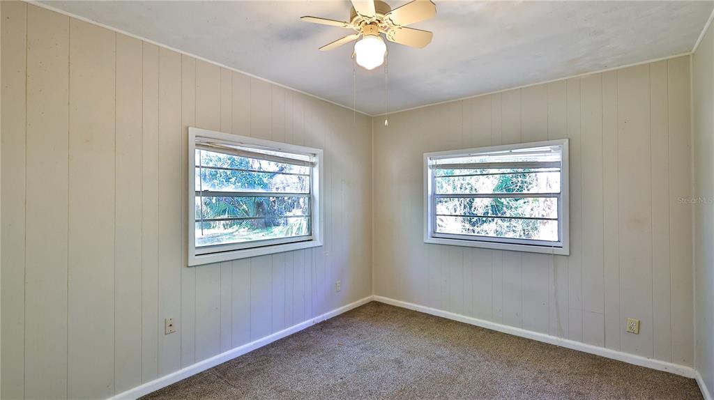 An empty bedroom features beige wood-paneled walls, brown carpet, and a ceiling fan — 5150 N OCEAN SHORE BOULEVARD, PALM COAST, FL