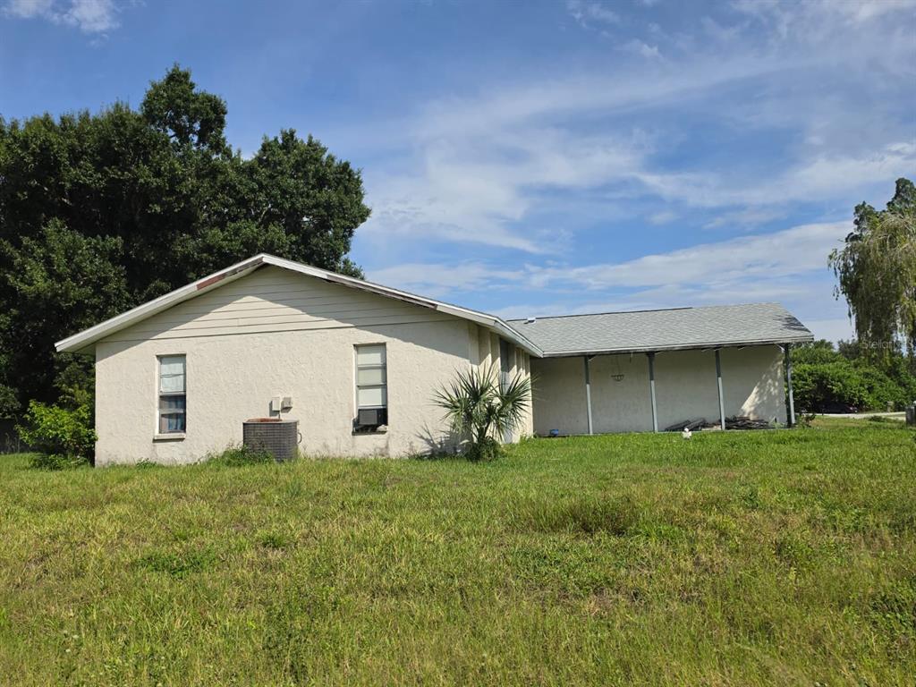 A single-story house with a stucco exterior, a covered side porch, and an overgrown lawn — 586 ALTOONA STREET NW, PORT CHARLOTTE, FL