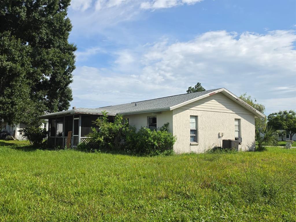 A single-story house with a screened-in porch and a large, grassy yard under a blue sky — 586 ALTOONA STREET NW, PORT CHARLOTTE, FL