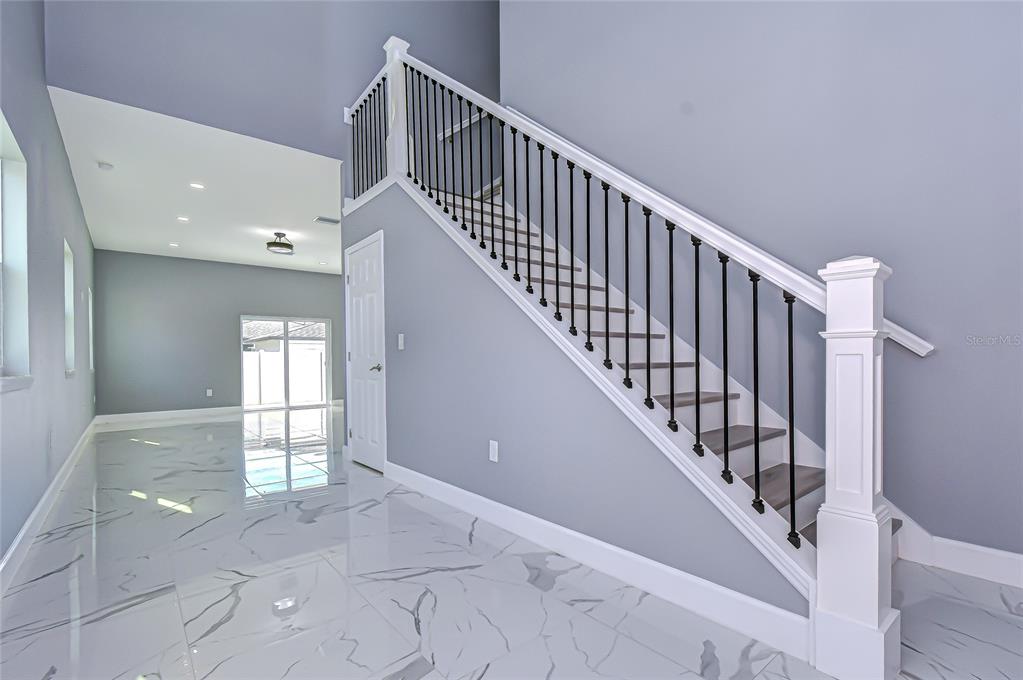 A staircase with black metal balusters and white trim sits above white marble-look tile flooring — 5312 76TH AVENUE N, PINELLAS PARK, FL