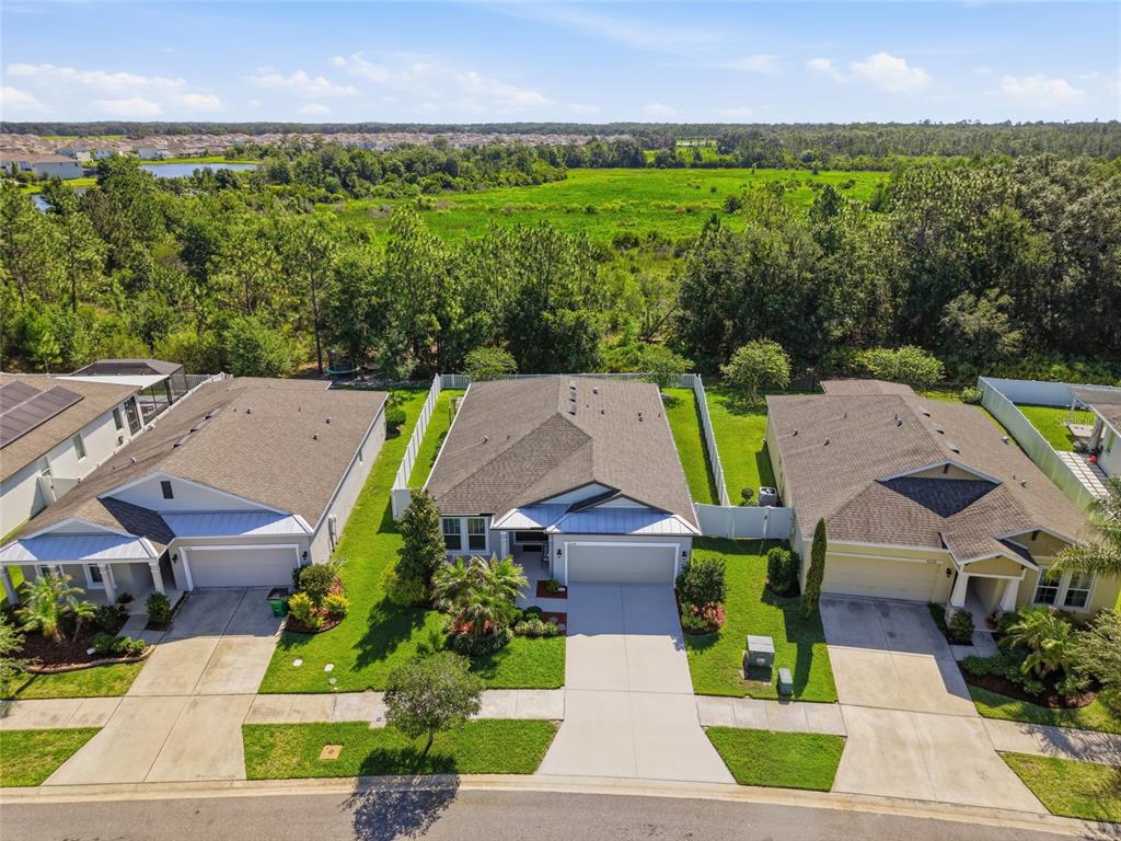 An aerial view shows three suburban houses with driveways and lawns facing a large field — 5234 TURTLE BAY DRIVE, WESLEY CHAPEL, FL