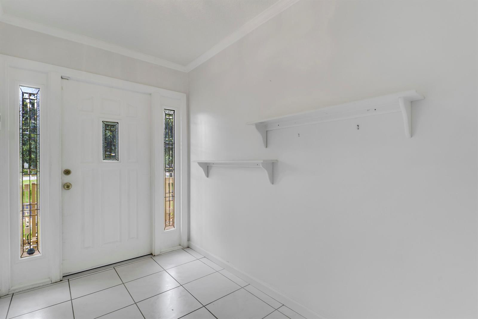 An entryway features white walls, tiled flooring, a front door with sidelights, and two wall-mounted shelves — 6824 Lakeside Road, West Palm Beach FL 33411, WEST PALM BEACH, FL