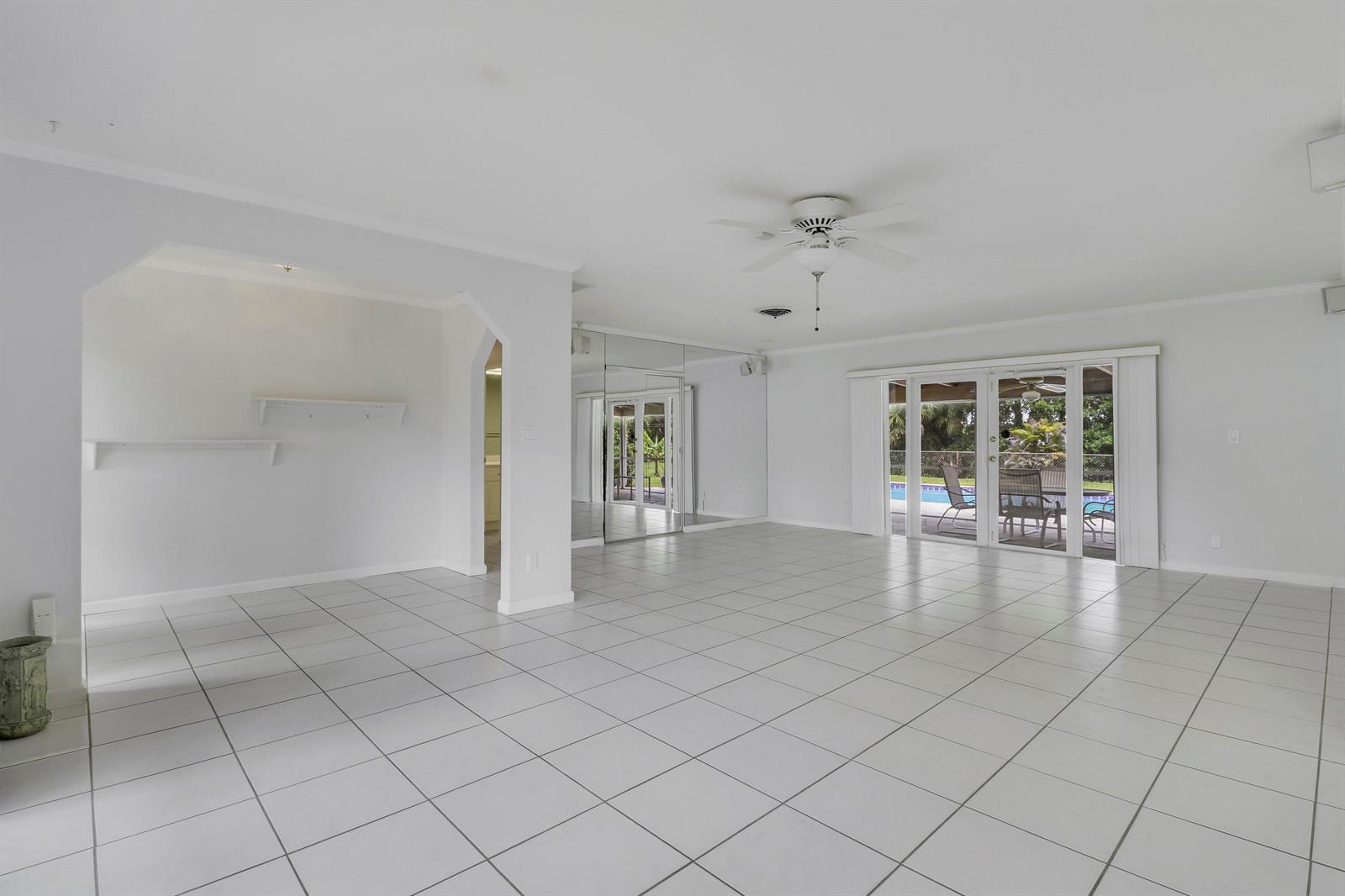 A bright, tiled living room features mirrored walls, a ceiling fan, and sliding glass doors — 6824 Lakeside Road, West Palm Beach FL 33411, WEST PALM BEACH, FL