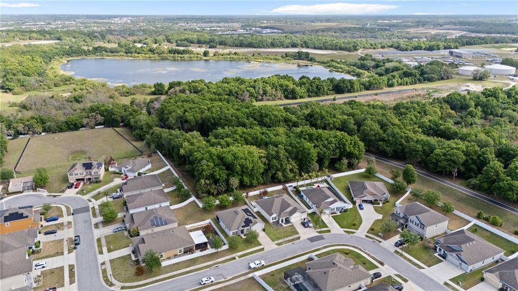 An aerial view shows a suburban neighborhood with houses bordering a large wooded area and lake — 3609 APOPKA RIDGE CIR, APOPKA, FL