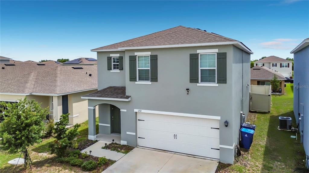 A two-story, light gray suburban house with a two-car garage and a covered entryway — 1172 CASCADES AVENUE, DAVENPORT, FL