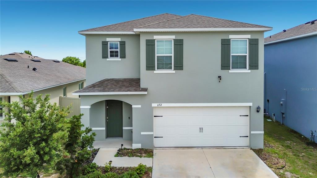A two-story house with a light green exterior, a white garage door, and dark shutters — 1172 CASCADES AVENUE, DAVENPORT, FL