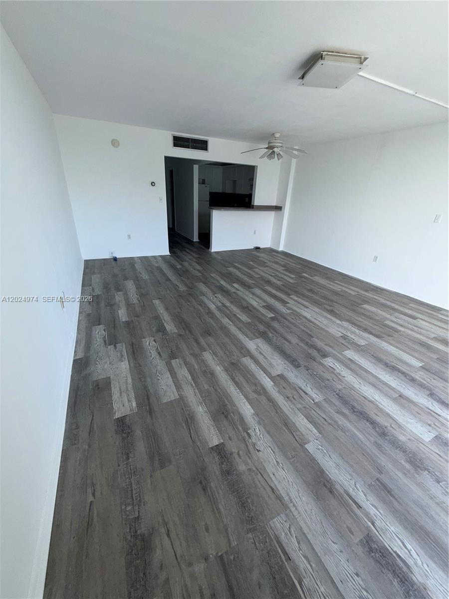 An empty living area features gray wood-look flooring, white walls, and a pass-through kitchen counter — 1470 NE 125th Ter # 605, North Miami FL 33161, NORTH MIAMI, FL