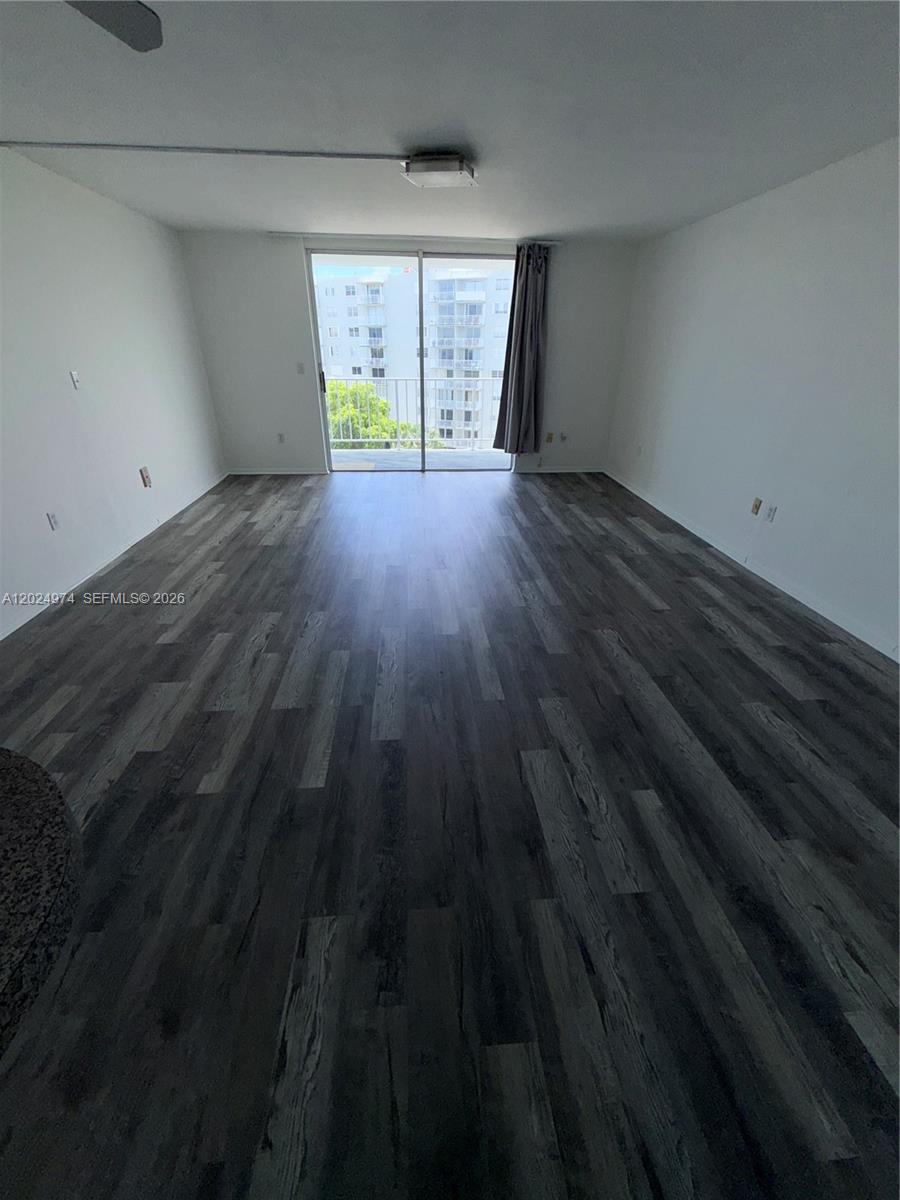 This empty room features dark wood-look flooring, white walls, and a sliding glass balcony door — 1470 NE 125th Ter # 605, North Miami FL 33161, NORTH MIAMI, FL