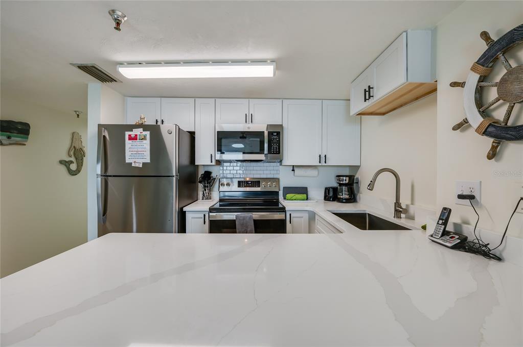 A kitchen features white cabinets, stainless steel appliances, and a white quartz countertop island — 3647 S ATLANTIC AVENUE UNIT 5B, DAYTONA BEACH, FL